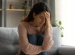 A woman sitting on a couch in deep thought, symbolizing emotional pain and relationship trauma.