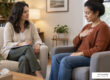 Licensed therapist guiding a seated adult client through a gentle somatic grounding exercise in a calm counseling office
